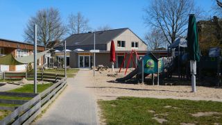 Au&szlig;engel&auml;nde des Ev. Kindergartens Husby mit Spielger&auml;ten, Sandfl&auml;che und dem Zugang zum Haupteingang